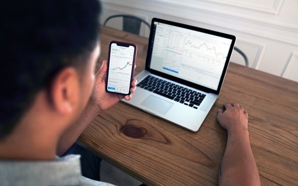 homme assis devant son ordinateur avec des graphiques sur son mobile et son écran d'ordinateur