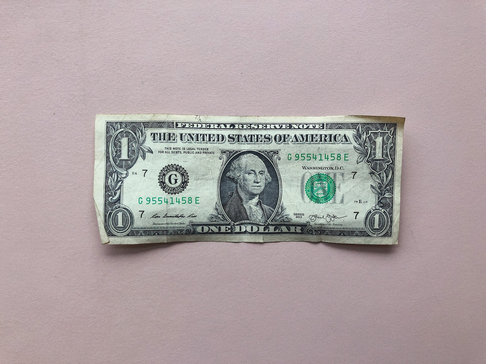 Un billet d'un dollar sur une surface rose.