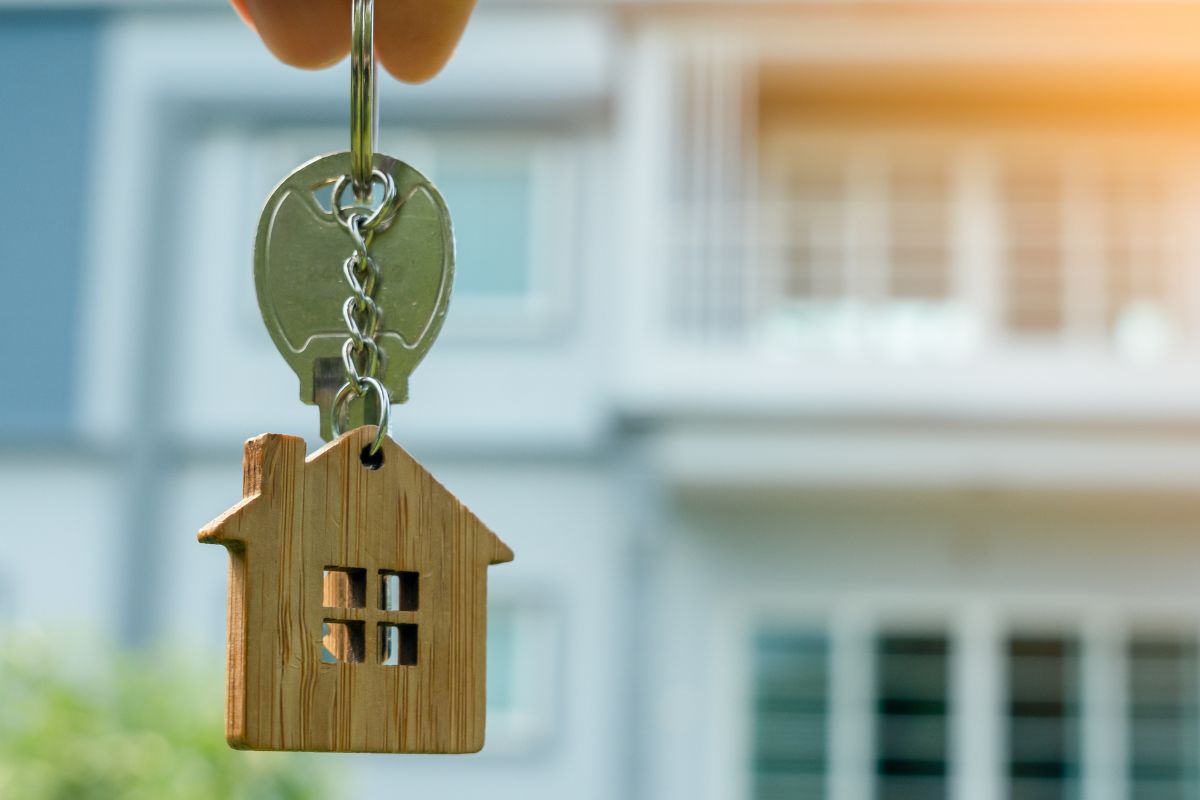 Une personne tenant une clé de maison en bois devant une maison.