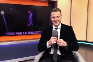 Homme en costume noir tenant un micro dans un studio